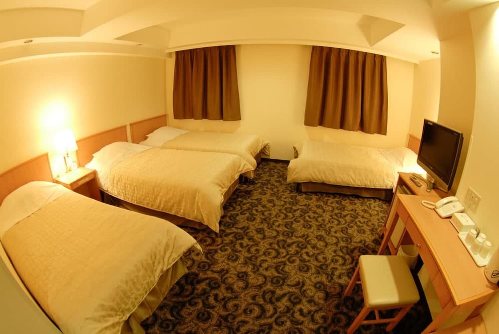 A cozy hotel room with warm lighting, neatly arranged twin beds, a desk with a TV, and patterned carpeting creates an inviting atmosphere ideal for travelers seeking comfort and relaxation.