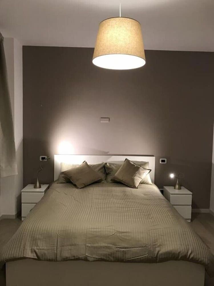 A cozy bedroom with a neatly made bed, soft lighting from a hanging lamp, and minimalist decor creates a serene atmosphere ideal for relaxation and sleep during travel.