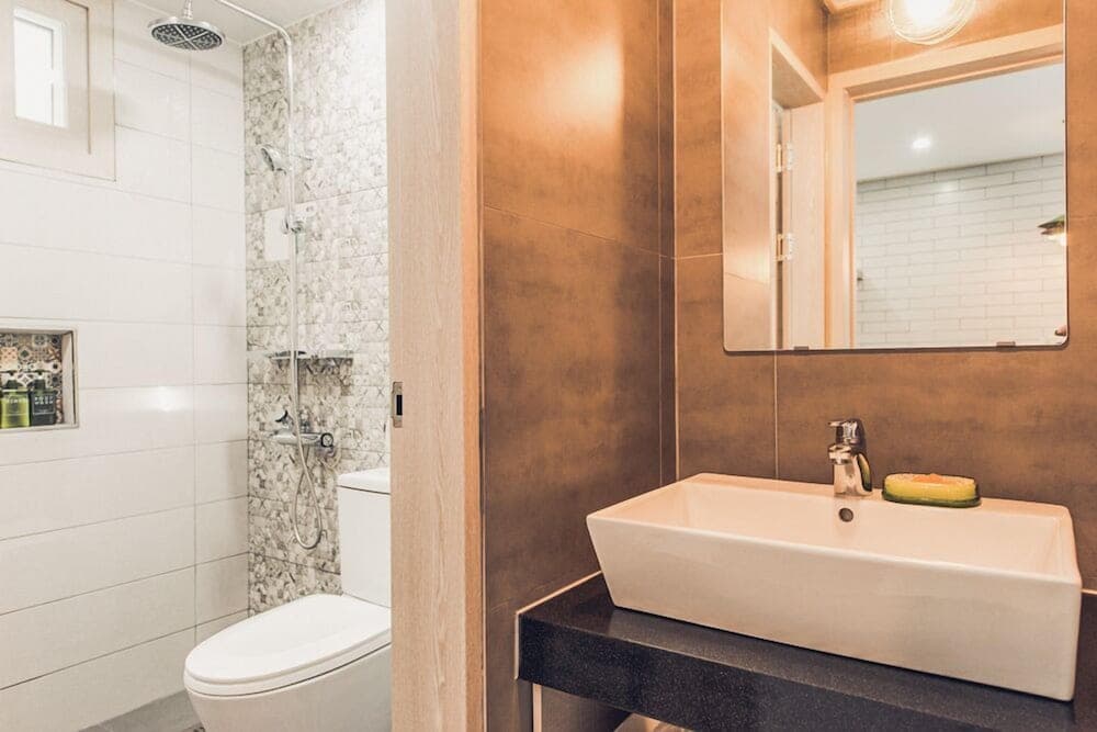 A modern bathroom with sleek white fixtures, a walk-in shower, and a minimalist sink setup offers a clean and inviting space ideal for travelers seeking comfort and style in their accommodations.