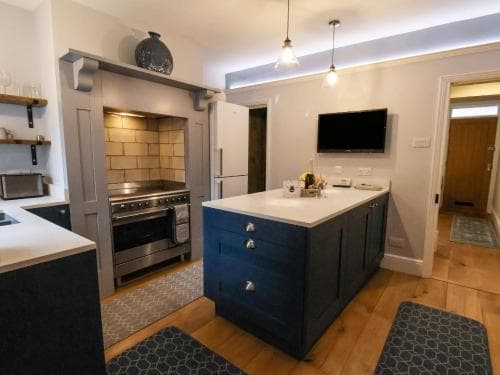A cozy, modern kitchen with wooden floors, a blue island, stainless steel appliances, and ambient lighting creates an inviting atmosphere ideal for travelers seeking a comfortable self-catering stay.