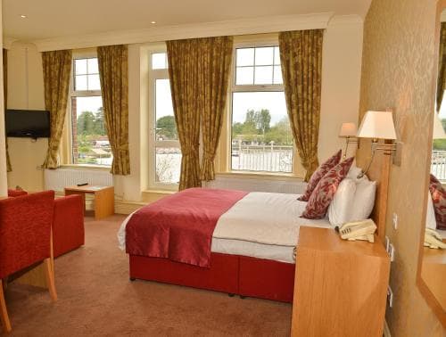 A cozy hotel room with a neatly made bed, warm-toned curtains, and a scenic view through large windows, ideal for travelers seeking comfort and relaxation.