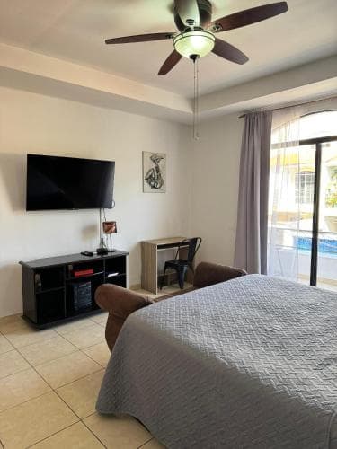 A cozy hotel room with a neatly made bed, flat-screen TV, and a view of a poolside area through a sliding glass door, ideal for travelers seeking comfort and relaxation.