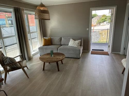 A cozy living room with a modern sofa, wooden coffee table, and large windows inviting natural light, creates a serene atmosphere ideal for a relaxing vacation rental stay.