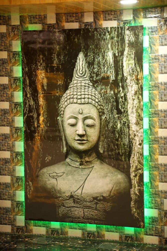 A serene Buddha statue mural framed by mosaic tiles and green lighting creates a tranquil ambiance in a spa or wellness center, ideal for relaxation and meditation.