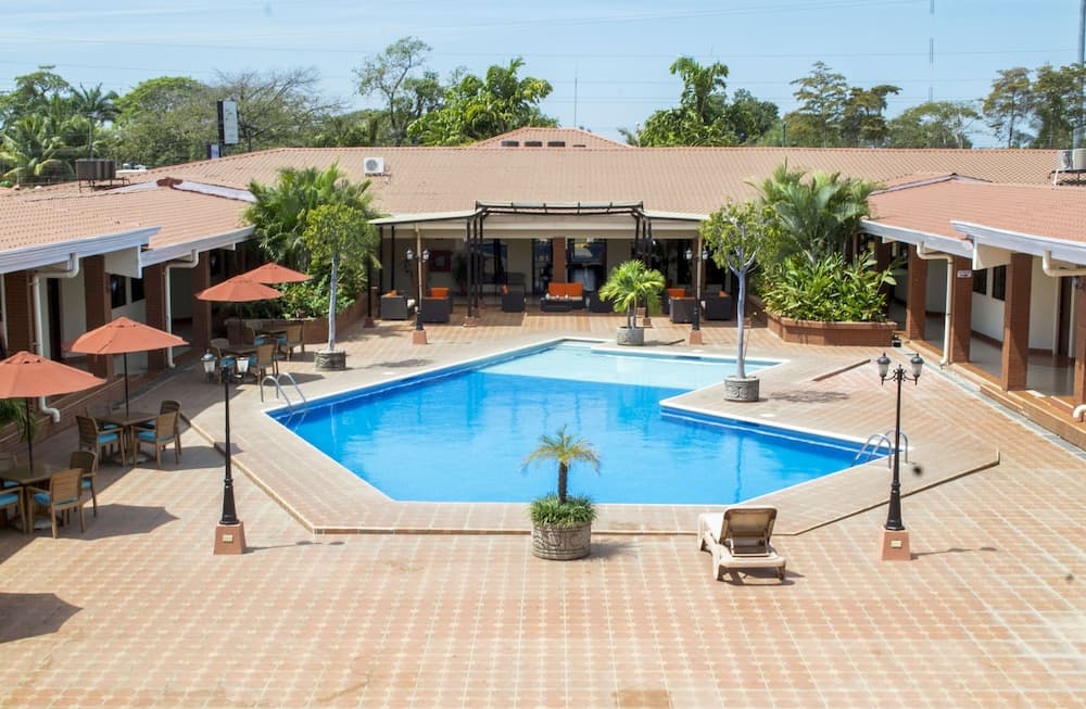 A serene tropical resort features a vibrant blue pool surrounded by lounge chairs, umbrellas, lush greenery, and a cozy patio area, ideal for travelers seeking relaxation and leisure.