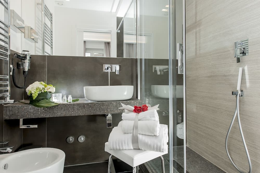 A luxurious hotel bathroom features sleek modern fixtures, a glass-enclosed shower, neatly folded towels adorned with red roses, and a serene ambiance ideal for relaxation and rejuvenation.