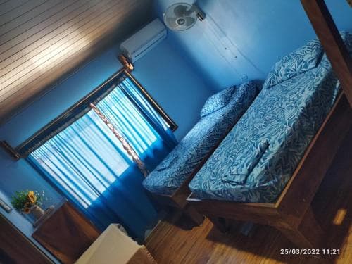 A cozy, blue-themed bedroom with patterned bedding, wooden furniture, and a window with curtains, evokes a serene and inviting atmosphere ideal for travelers seeking a comfortable stay.