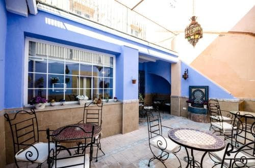 A charming courtyard with blue walls, mosaic tables, and ornate lanterns creates an inviting atmosphere perfect for travelers seeking a cozy outdoor dining or relaxation spot.