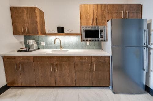 A modern kitchen with wooden cabinets, a stainless steel refrigerator, and a tiled backsplash offers a cozy and functional space ideal for travelers seeking self-catering accommodations.