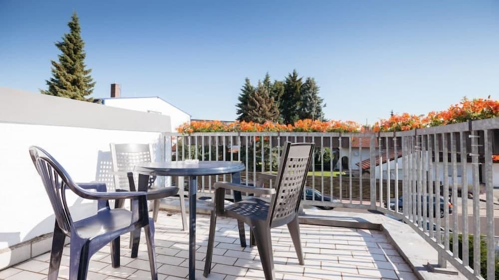 A serene rooftop terrace features a cozy seating area with metal chairs and a table, surrounded by vibrant orange flowers and lush greenery, ideal for travelers seeking a peaceful retreat in an urban setting.