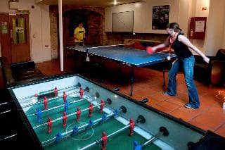 A cozy indoor recreational area features a lively game of table tennis and foosball, creating an inviting atmosphere for travelers seeking entertainment and relaxation.