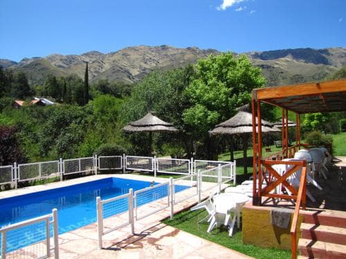 A serene mountain retreat features a vibrant blue pool surrounded by lush greenery, straw umbrellas, and cozy seating areas, ideal for relaxing vacations in nature.