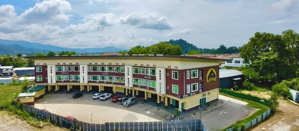 A serene aerial view of a modern multi-story building surrounded by lush greenery and mountains under a partly cloudy sky, ideal for travelers seeking accommodation in a tranquil, nature-rich environment.