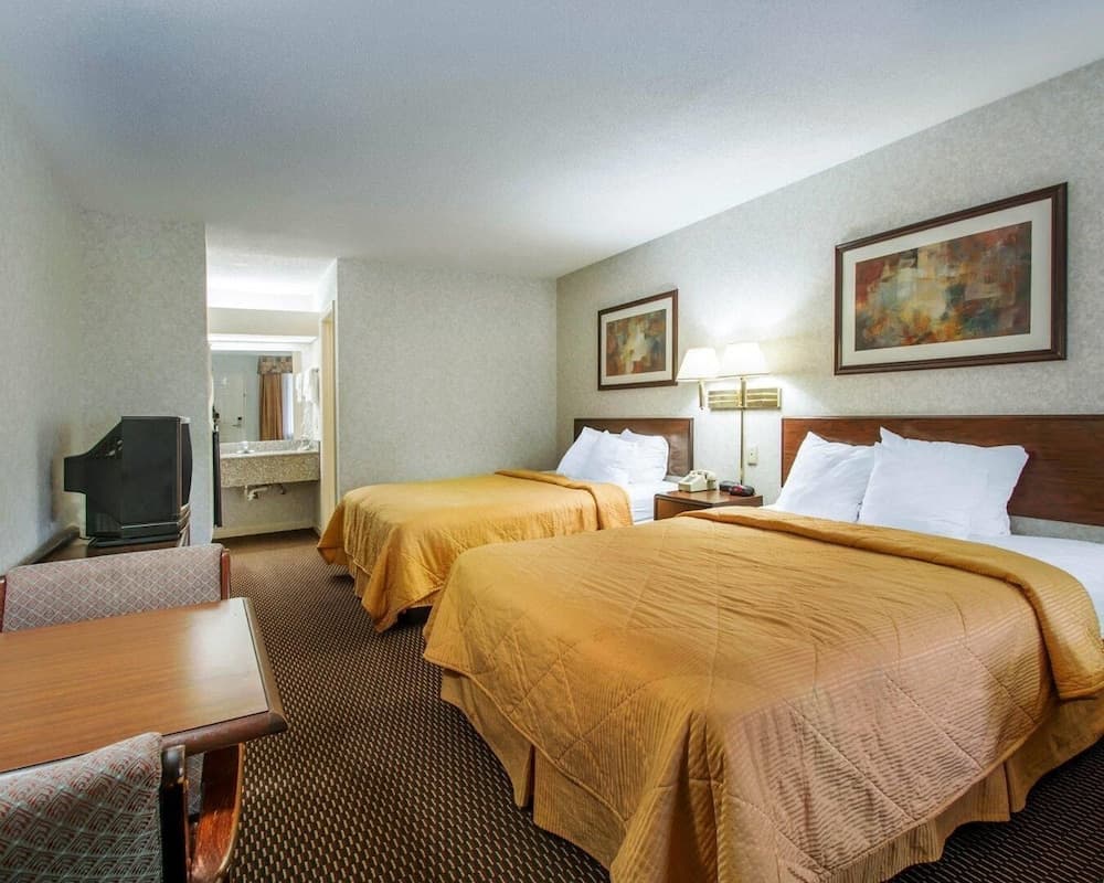 A cozy hotel room features two neatly made beds with yellow quilts, a small dining table, wall-mounted lamps, and abstract artwork, ideal for travelers seeking comfort and convenience.