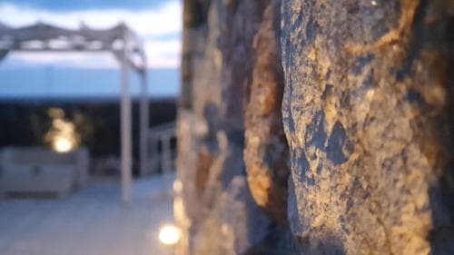A serene evening at an outdoor patio features a textured stone wall in the foreground, with soft lighting and a blurred pergola in the background, ideal for romantic getaways or tranquil retreats.