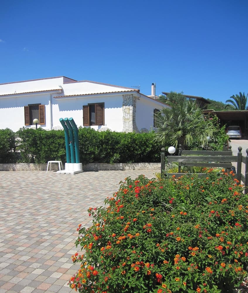 A serene Mediterranean villa courtyard features vibrant orange flowers, lush greenery, and modern art sculptures under a clear blue sky, ideal for a relaxing vacation retreat.