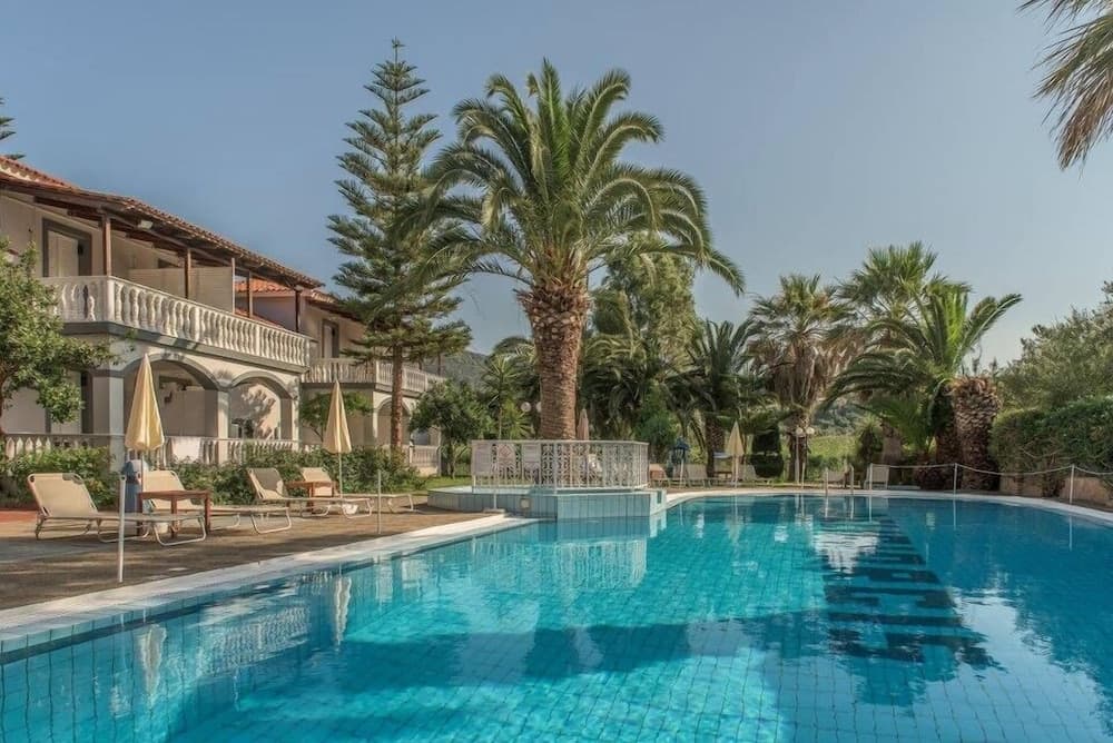 A serene resort pool surrounded by lush palm trees and a charming villa offers a tranquil escape for vacationers seeking relaxation under the sun.