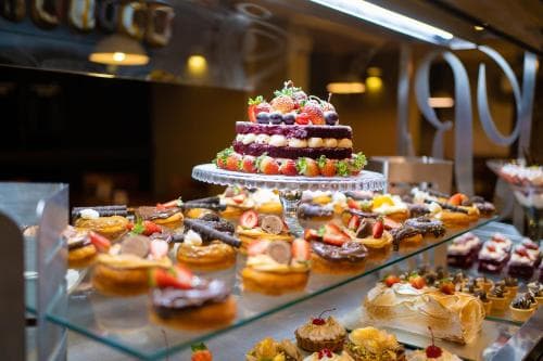 A vibrant display of assorted pastries and a layered fruit-topped cake in a cozy bakery setting evokes a delightful culinary adventure, perfect for travelers seeking local sweet treats.