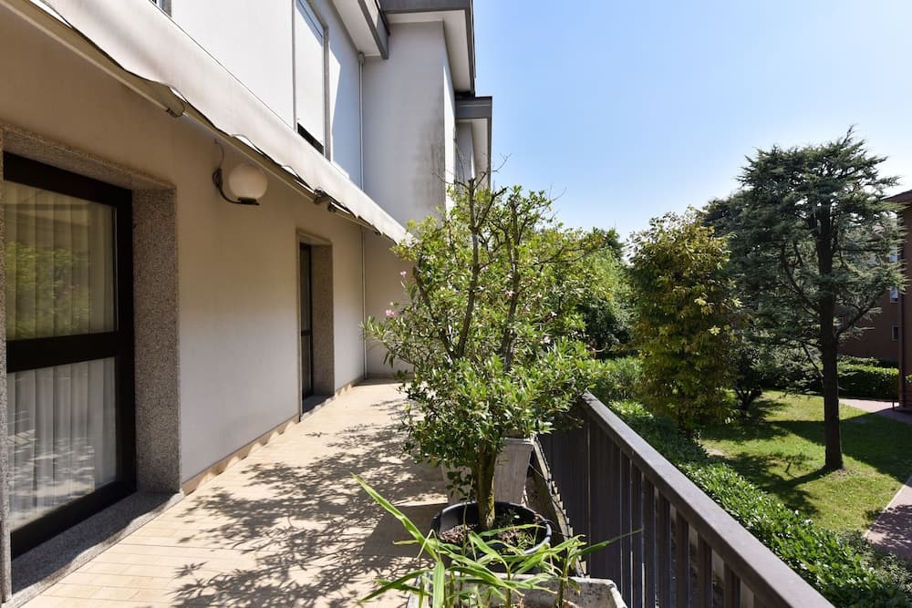 A serene residential balcony adorned with potted plants overlooks a lush green garden under a clear blue sky, ideal for travelers seeking a peaceful retreat.
