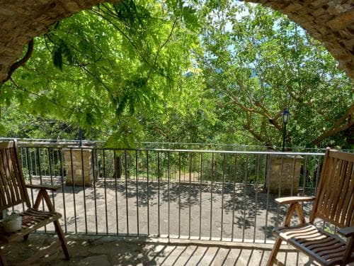 A serene balcony framed by lush greenery offers a tranquil retreat, perfect for travelers seeking relaxation amidst nature, with wooden chairs inviting guests to enjoy the peaceful ambiance.