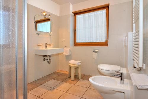A cozy, well-lit bathroom with tiled floors, dual sinks, a shower, and a wooden-framed window offers a serene space for travelers seeking comfort and cleanliness during their stay.