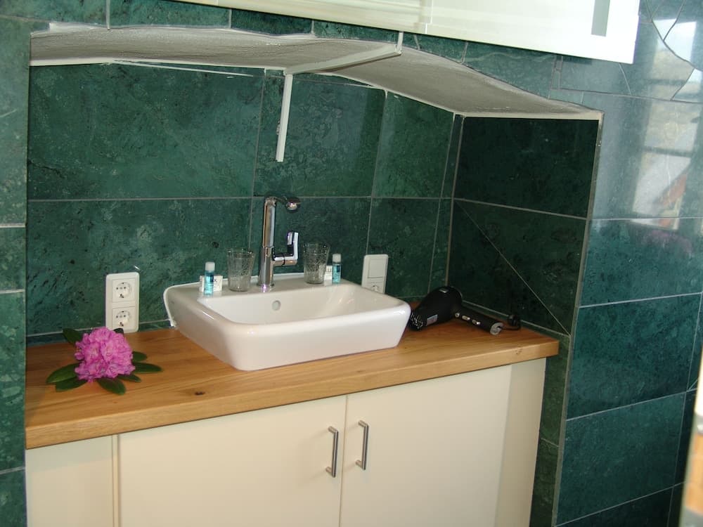 A cozy bathroom with green marble tiles features a white sink on a wooden countertop, adorned with a pink flower, creating a serene atmosphere ideal for travelers seeking comfort and style.