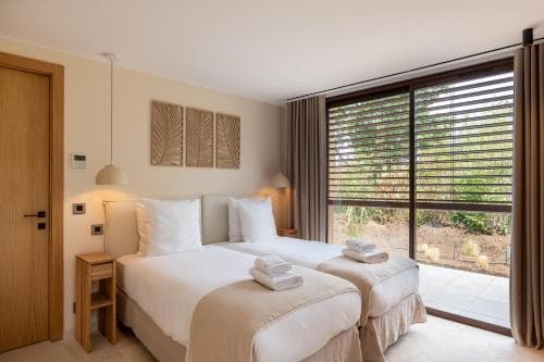 A serene hotel bedroom with a cozy bed, modern decor, and large windows overlooking lush greenery, ideal for travelers seeking relaxation and comfort.