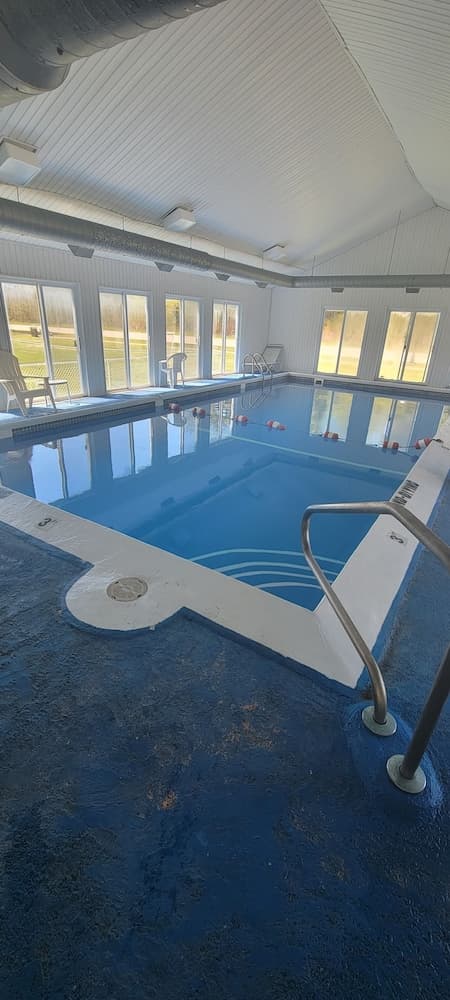 A serene indoor swimming pool with clear blue water, surrounded by large windows and lounge chairs, offers a tranquil retreat for relaxation and fitness activities.