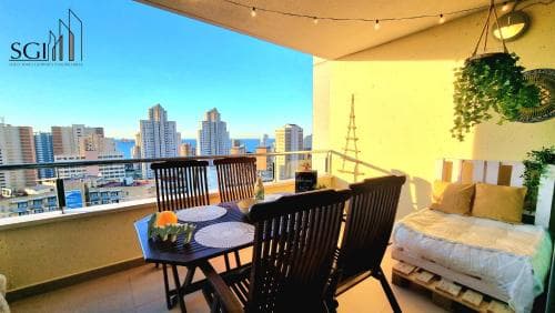 A cozy balcony with wooden furniture overlooks a vibrant city skyline under a clear blue sky, perfect for travelers seeking urban relaxation and scenic views.