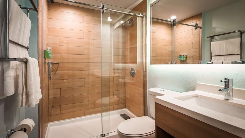 A modern bathroom with warm-toned tiled walls, a glass-enclosed shower, sleek fixtures, and soft lighting creates a cozy ambiance ideal for travelers seeking comfort and cleanliness.