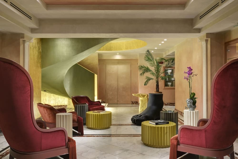 A luxurious hotel lobby features plush red armchairs, golden tables, and a striking black sculpture amidst warm-toned walls and marble floors, creating an inviting atmosphere ideal for relaxation and socializing.