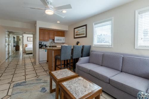 A cozy apartment living space features a tiled floor, gray sofa, wooden coffee tables, and an open kitchen area, ideal for travelers seeking comfort and convenience in a homey setting.