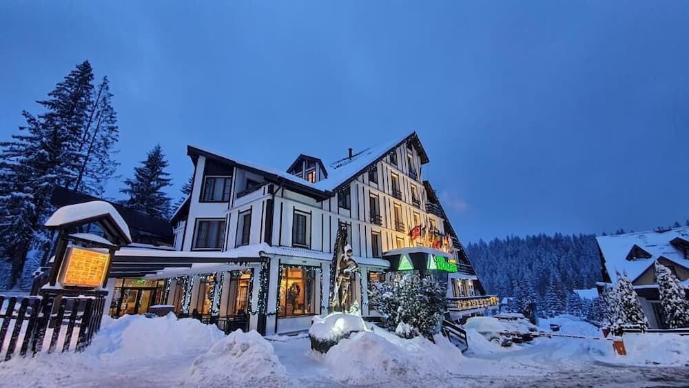 A cozy, snow-covered chalet-style hotel illuminated against the twilight sky offers a serene winter retreat, perfect for travelers seeking a picturesque alpine getaway.