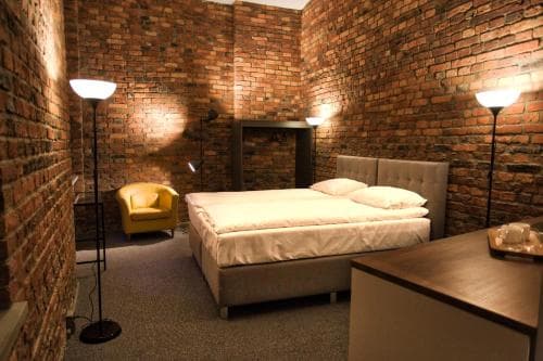 A cozy bedroom with exposed brick walls, warm lighting, and modern furnishings creates an inviting atmosphere ideal for travelers seeking a unique boutique hotel experience.