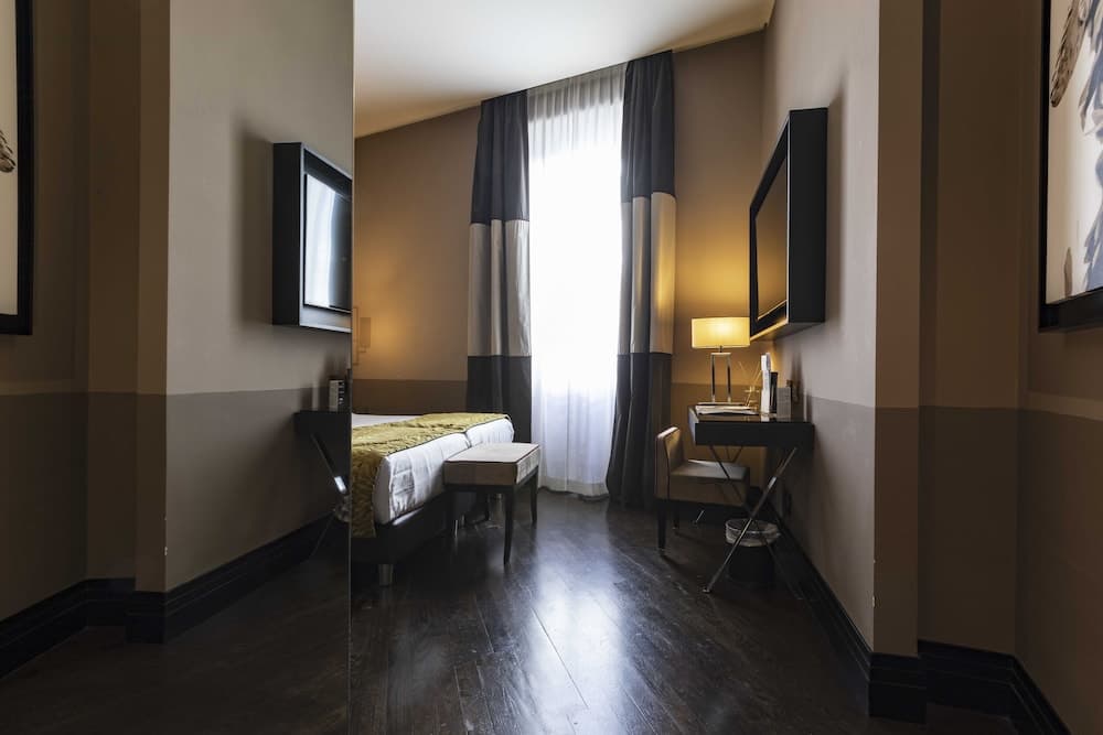 A cozy hotel room with warm lighting, dark wood floors, a neatly made bed, and a desk by the window, ideal for travelers seeking comfort and functionality.