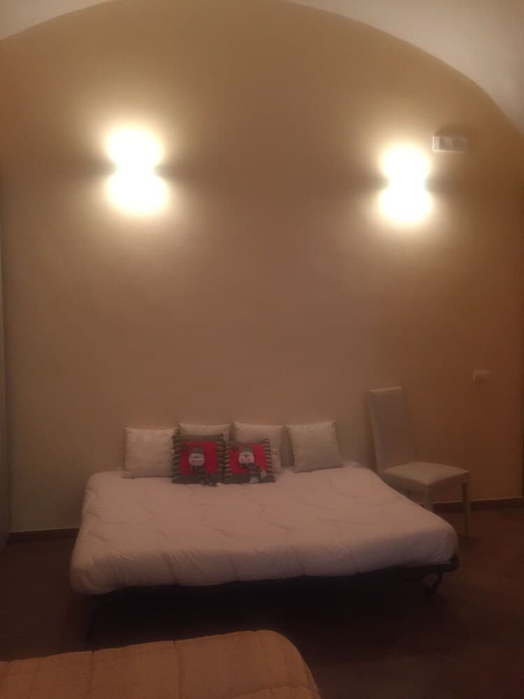 A cozy bedroom with a neatly made bed adorned with festive pillows under warm wall lights, ideal for travelers seeking a serene and inviting accommodation.