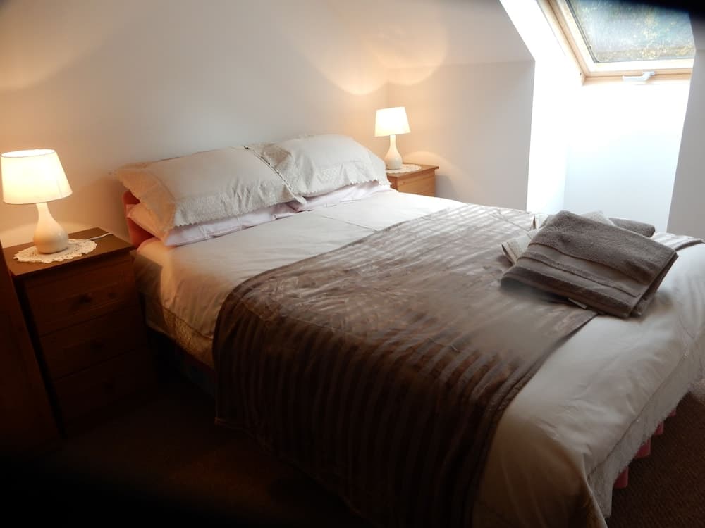 A cozy attic bedroom with soft lighting from bedside lamps, neatly arranged towels on the bed, and a skylight window, ideal for travelers seeking a serene and intimate accommodation experience.