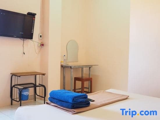 A cozy hotel room features a neatly made bed with folded blue towels, a small desk with a mirror, a wall-mounted TV, and minimalistic decor, ideal for travelers seeking a simple and comfortable stay.