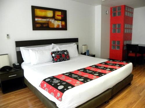 A cozy hotel room features a neatly made bed adorned with vibrant red and black bedding, complemented by modern artwork and a striking red wardrobe, creating an inviting atmosphere ideal for travelers seeking comfort and style.
