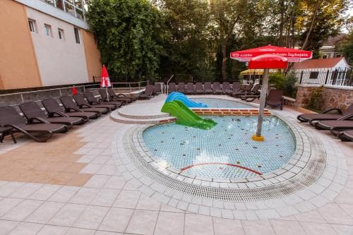 A vibrant outdoor pool area featuring a playful green slide, lounge chairs, and colorful umbrellas creates a relaxing and fun atmosphere ideal for family vacations or leisurely getaways.