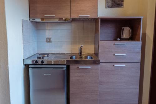 A cozy, compact kitchenette featuring wooden cabinets, a stainless steel sink, and a small stove, ideal for travelers seeking self-catering accommodations in an apartment or hotel setting.
