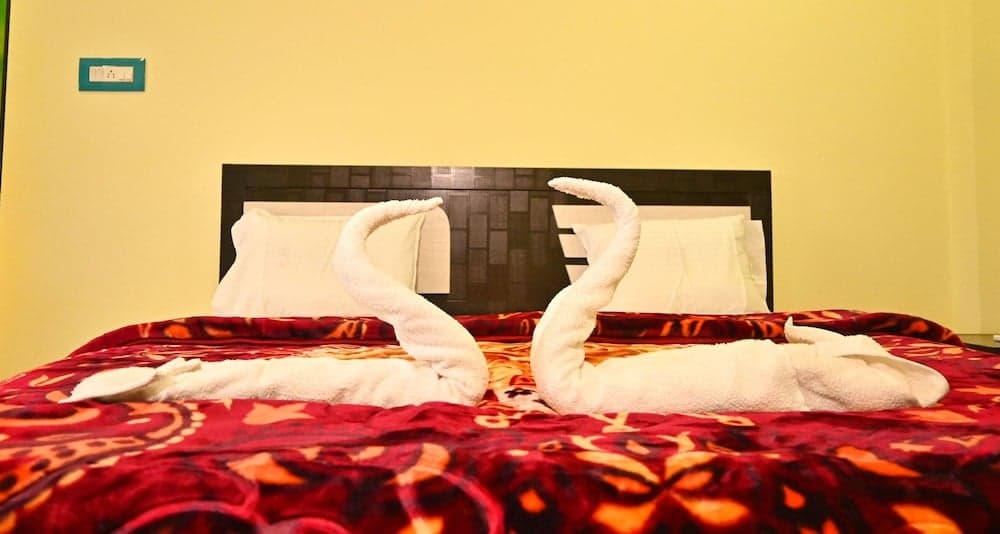 A cozy hotel room features a neatly made bed adorned with vibrant red bedding and creatively folded towel swans, evoking a welcoming and playful atmosphere ideal for travelers seeking comfort and charm.