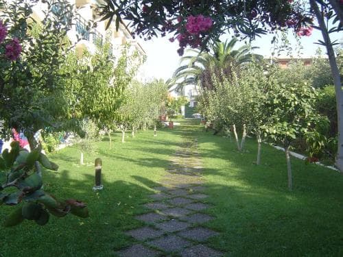 A serene garden pathway lined with lush greenery and blooming trees invites travelers to explore a tranquil resort setting, perfect for relaxation and leisurely strolls.
