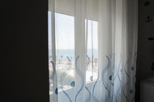 A serene coastal view framed by sheer curtains with wave patterns invites travelers to relax in a beachside accommodation, perfect for a tranquil seaside getaway.