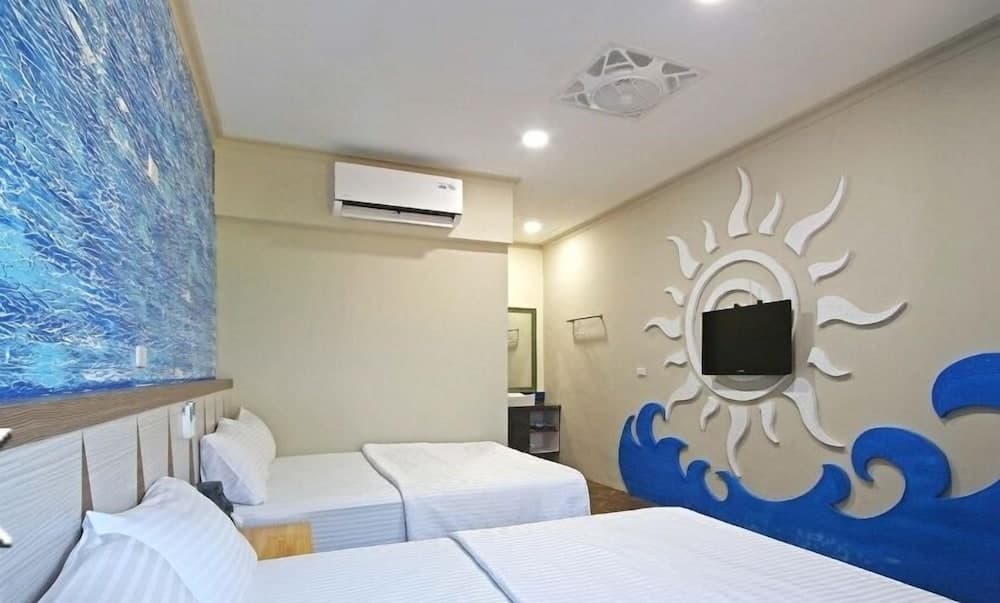 A cozy hotel room with twin beds, a vibrant ocean-themed mural, and a sun design on the wall offers a relaxing seaside ambiance ideal for travelers seeking comfort and thematic decor.
