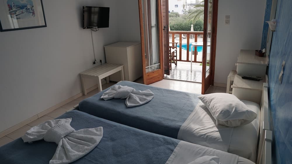 A cozy hotel room with neatly arranged twin beds, a balcony overlooking a serene poolside view, and a tranquil atmosphere ideal for a relaxing getaway.