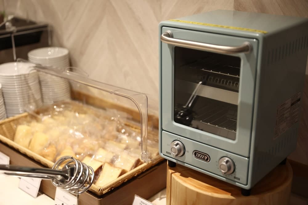 A cozy hotel breakfast area features a sleek toaster oven beside a basket of neatly arranged bread slices, inviting travelers to enjoy a warm start to their day.