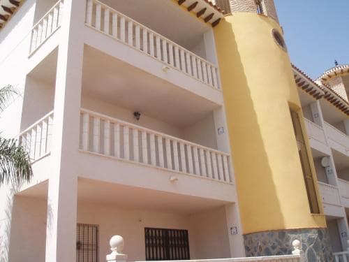 A sunny Mediterranean-style apartment complex with pastel-colored facades, balconies, and tiled roofs offers a serene vacation retreat ideal for travelers seeking coastal charm.