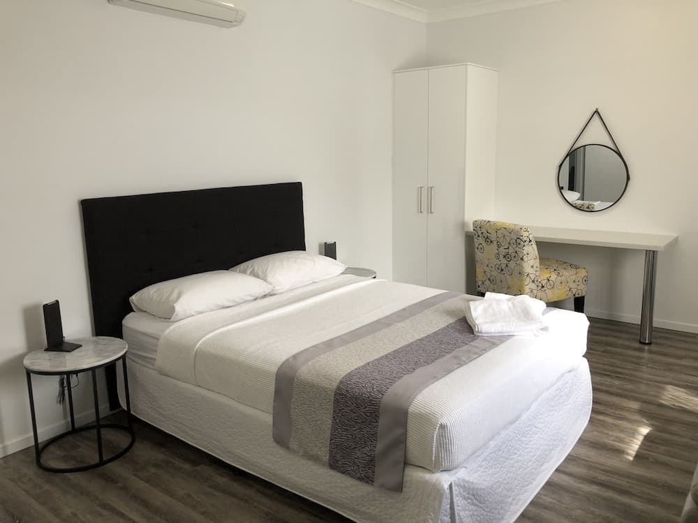 A cozy hotel room features a neatly made bed with white linens, a black headboard, a stylish desk with a bicycle-patterned chair, and a modern mirror, ideal for travelers seeking comfort and simplicity.