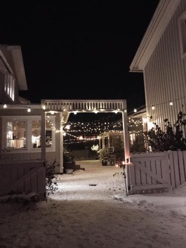 A cozy winter evening scene features a snow-covered courtyard illuminated by string lights, creating a serene and inviting atmosphere ideal for holiday retreats or romantic getaways.